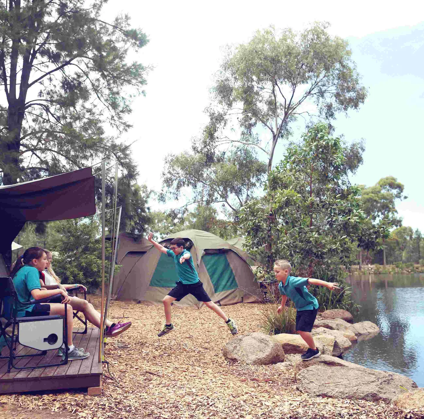 Students enjoying outdoor activities near safari‑style tents during a Zoosnooz overnight education program. near billabong